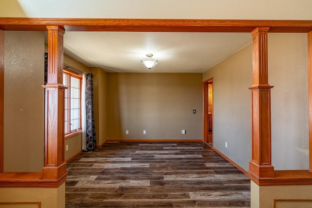 spare room with baseboards, ornate columns, and dark wood finished floors