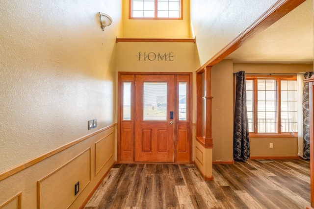 foyer entrance with a decorative wall, dark wood-type flooring, a wainscoted wall, and a healthy amount of sunlight