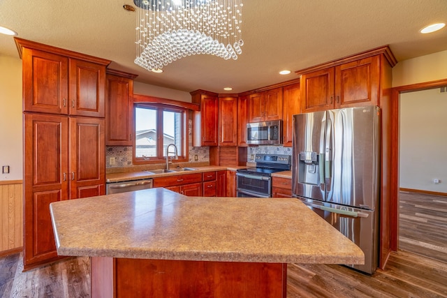 kitchen featuring a sink, brown cabinets, wainscoting, stainless steel appliances, and dark wood-type flooring