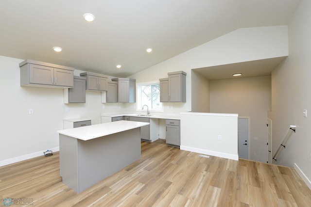 kitchen featuring vaulted ceiling, gray cabinets, a sink, light wood-style floors, and a center island