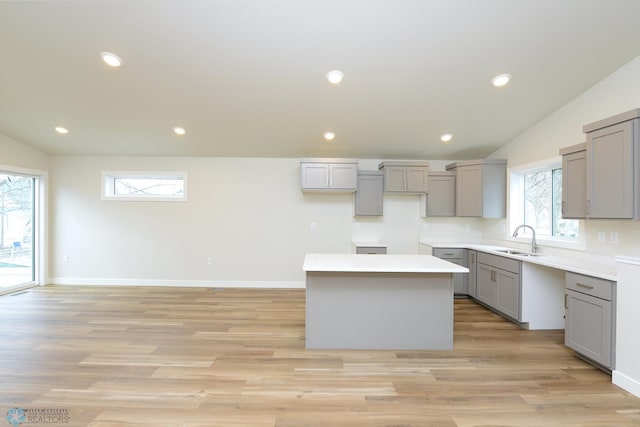 kitchen with lofted ceiling, light wood finished floors, gray cabinets, a sink, and a kitchen island