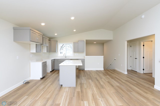 kitchen with gray cabinets, vaulted ceiling, a center island, and light wood-type flooring