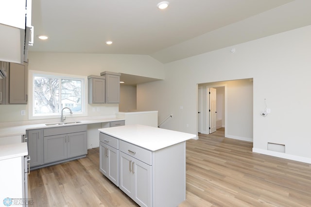 kitchen featuring lofted ceiling, a sink, light wood-style floors, and gray cabinets