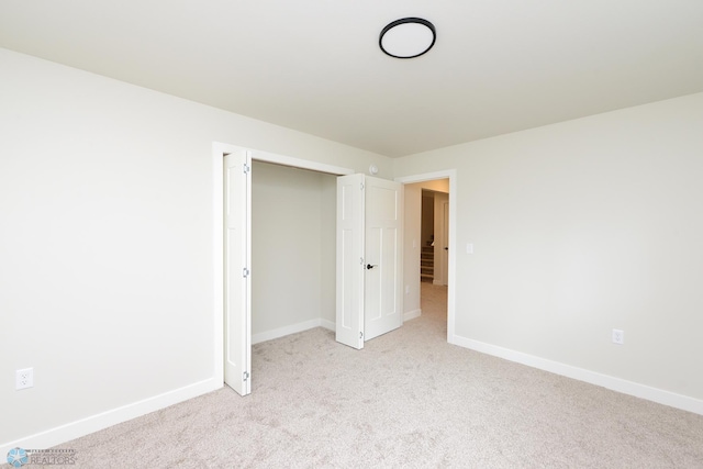 unfurnished bedroom with light carpet, a closet, and baseboards