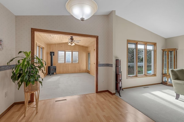 entrance foyer featuring a wood stove, baseboards, lofted ceiling, light wood-type flooring, and visible vents