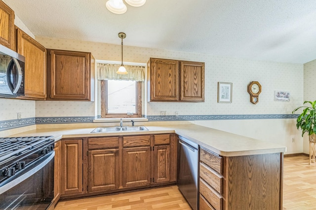 kitchen featuring a peninsula, wallpapered walls, light wood-type flooring, a sink, and stainless steel appliances