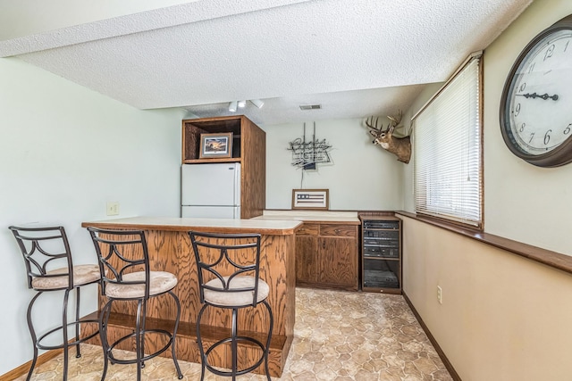 bar with bar, beverage cooler, a textured ceiling, freestanding refrigerator, and visible vents