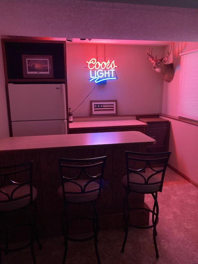 bar featuring baseboards and freestanding refrigerator