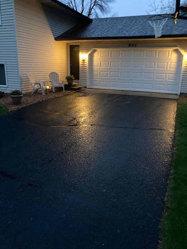 exterior space with an attached garage, a shingled roof, and aphalt driveway