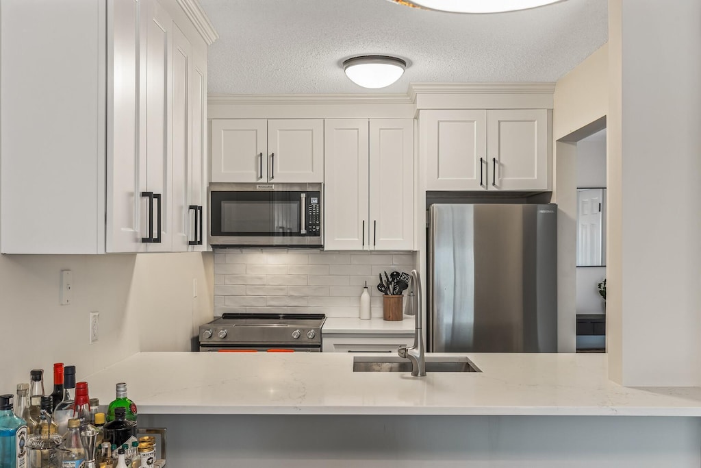 kitchen featuring light stone countertops, tasteful backsplash, a peninsula, a textured ceiling, and stainless steel appliances