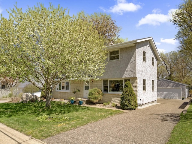 view of front of house with an outdoor structure, a detached garage, brick siding, stucco siding, and a front lawn