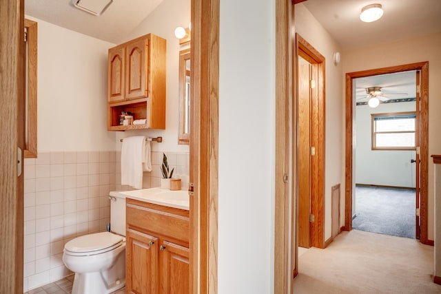 bathroom with a ceiling fan, tile walls, toilet, wainscoting, and vanity