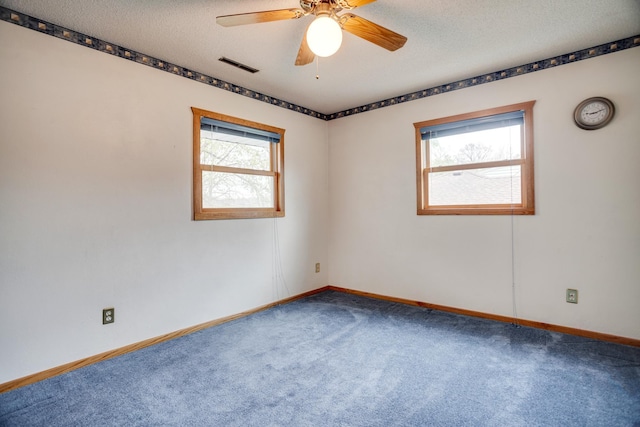 carpeted spare room featuring a wealth of natural light, visible vents, baseboards, and ceiling fan