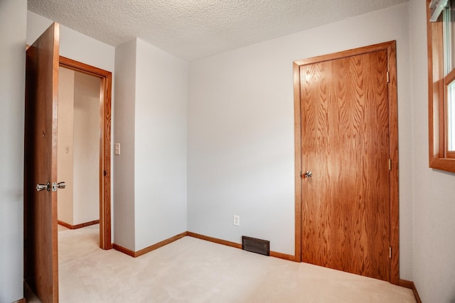 unfurnished room with baseboards, light carpet, visible vents, and a textured ceiling