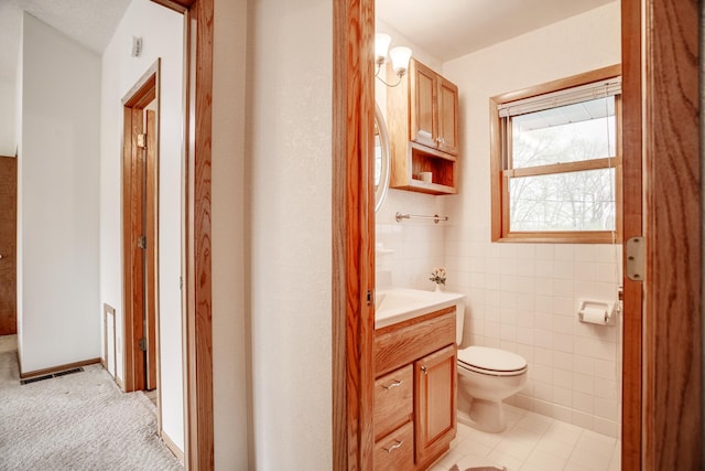 half bathroom featuring vanity, toilet, tile walls, and visible vents
