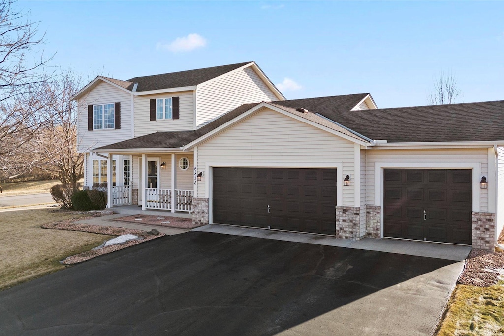 traditional home with a porch, a shingled roof, a garage, and aphalt driveway