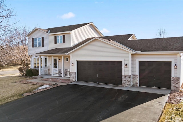 traditional home with a porch, a shingled roof, a garage, and aphalt driveway