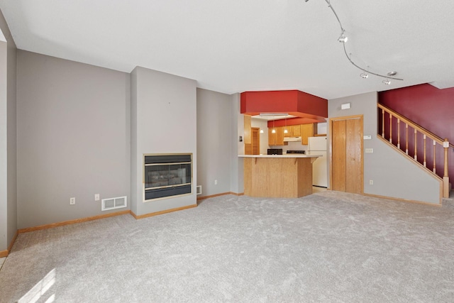 unfurnished living room featuring stairs, a glass covered fireplace, light carpet, baseboards, and visible vents