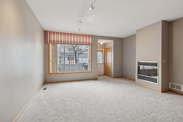 unfurnished living room with visible vents, track lighting, carpet flooring, and a textured ceiling