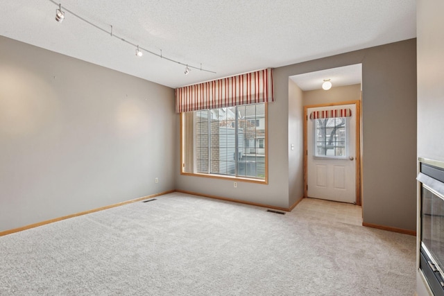 interior space featuring a textured ceiling, baseboards, visible vents, carpet, and track lighting