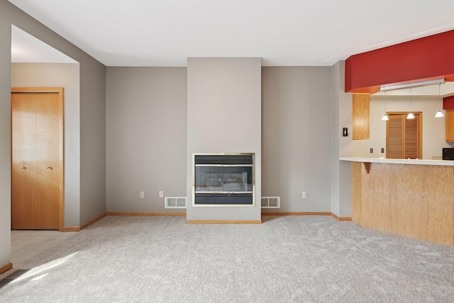 unfurnished living room with a glass covered fireplace, baseboards, visible vents, and carpet floors