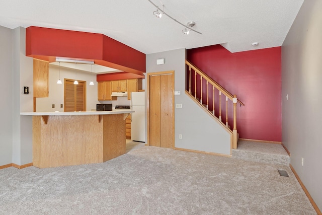 kitchen featuring under cabinet range hood, visible vents, freestanding refrigerator, a peninsula, and light colored carpet