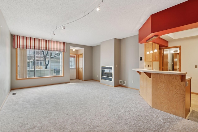unfurnished living room featuring track lighting, light carpet, visible vents, and baseboards