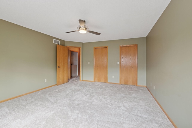unfurnished bedroom with light carpet, baseboards, visible vents, a ceiling fan, and two closets