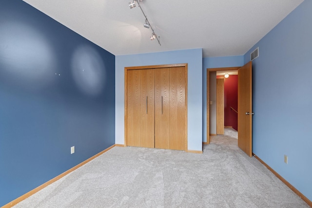 unfurnished bedroom featuring baseboards, carpet floors, a closet, and rail lighting