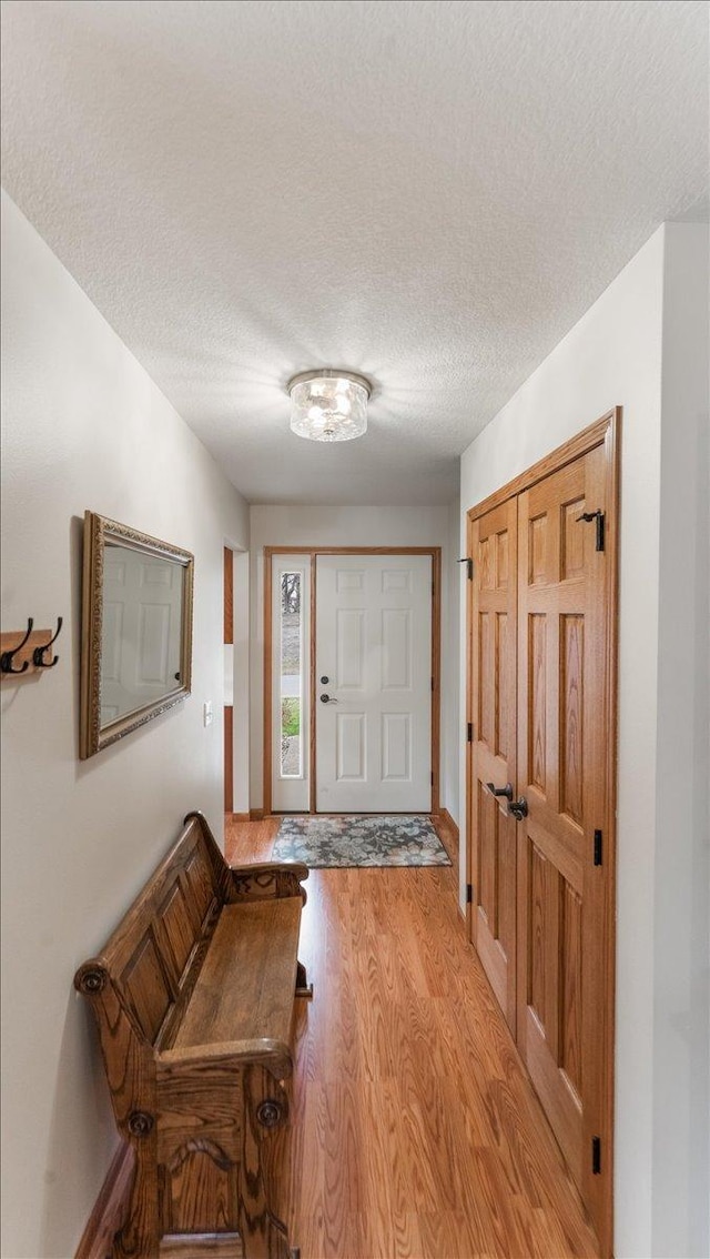 foyer entrance with a textured ceiling, baseboards, and light wood-style flooring