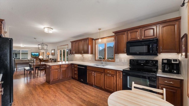 kitchen featuring hanging light fixtures, light countertops, a peninsula, tasteful backsplash, and black appliances