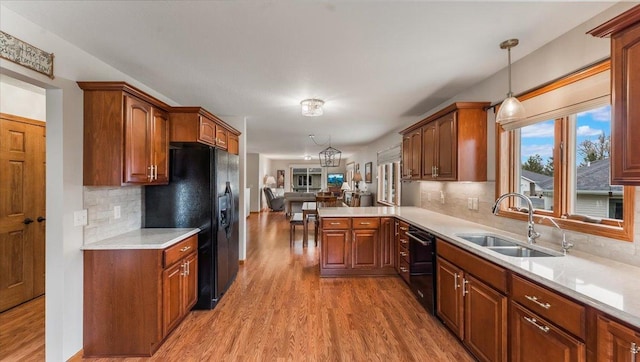 kitchen featuring open floor plan, light countertops, a sink, light wood finished floors, and black appliances