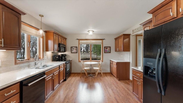 kitchen featuring a sink, light countertops, light wood-style flooring, tasteful backsplash, and black appliances