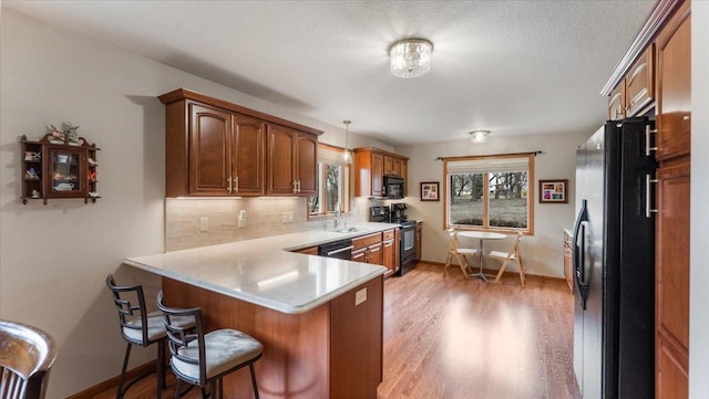 kitchen featuring decorative backsplash, a peninsula, light countertops, a sink, and black appliances