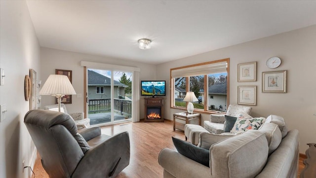 living room with baseboards, a lit fireplace, and light wood finished floors
