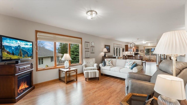 living room with a warm lit fireplace and light wood-style flooring