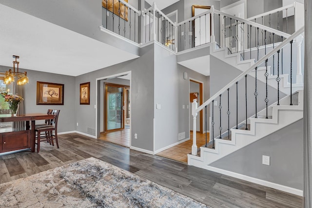 foyer entrance featuring stairs, a towering ceiling, wood finished floors, baseboards, and a notable chandelier