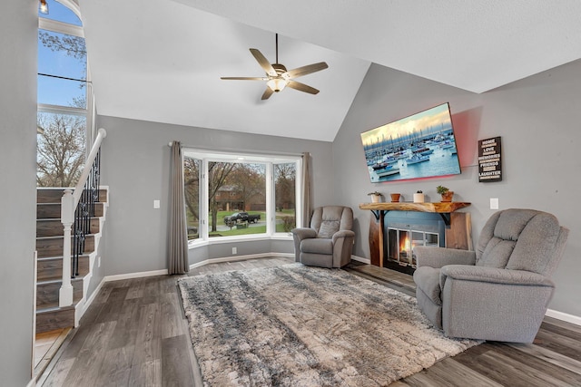 living room featuring ceiling fan, a glass covered fireplace, wood finished floors, and stairway