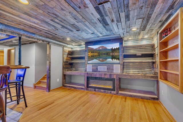 interior space featuring stairs, a glass covered fireplace, wood finished floors, baseboards, and wood ceiling