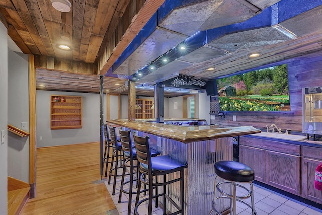 bar with wooden walls, indoor bar, light wood-type flooring, black stovetop, and a sink