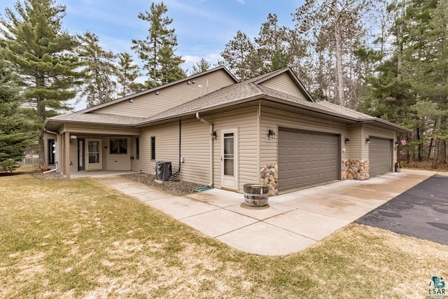 view of side of property featuring aphalt driveway, central AC, a yard, an attached garage, and a shingled roof
