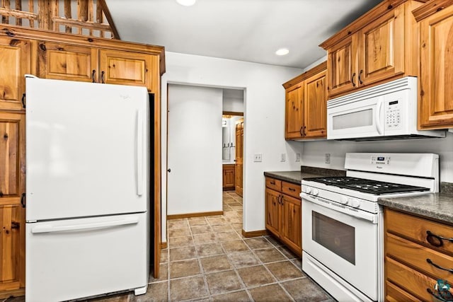 kitchen with brown cabinetry, dark countertops, and white appliances