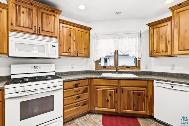 kitchen with recessed lighting, white appliances, dark countertops, brown cabinets, and a sink