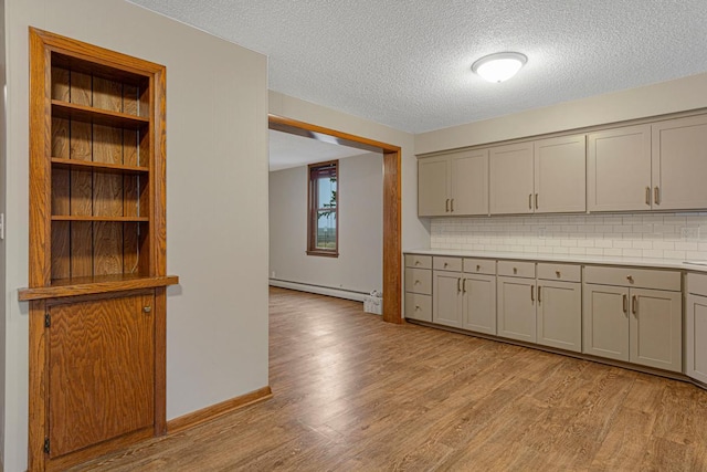 kitchen featuring light wood-style flooring, a textured ceiling, backsplash, gray cabinetry, and a baseboard radiator
