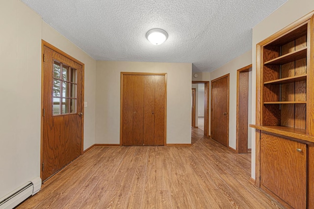 unfurnished bedroom featuring baseboard heating, baseboards, light wood-style floors, and a textured ceiling