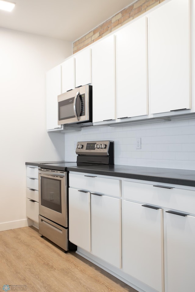 kitchen featuring tasteful backsplash, white cabinetry, dark countertops, stainless steel appliances, and light wood finished floors