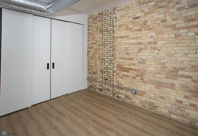 unfurnished bedroom with brick wall, wood finished floors, and a closet