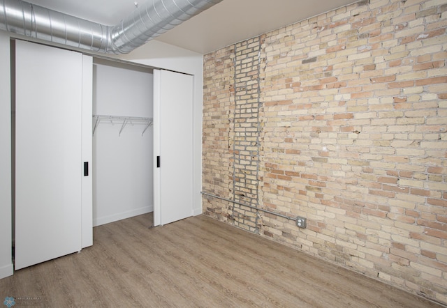 unfurnished bedroom with brick wall, wood finished floors, and a closet