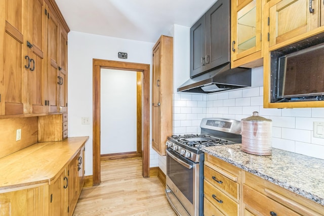 kitchen featuring stainless steel gas range, under cabinet range hood, light wood-style flooring, decorative backsplash, and light stone counters