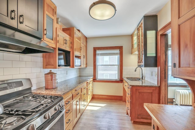 kitchen with stainless steel gas range oven, radiator heating unit, a sink, baseboards, and light wood-style flooring